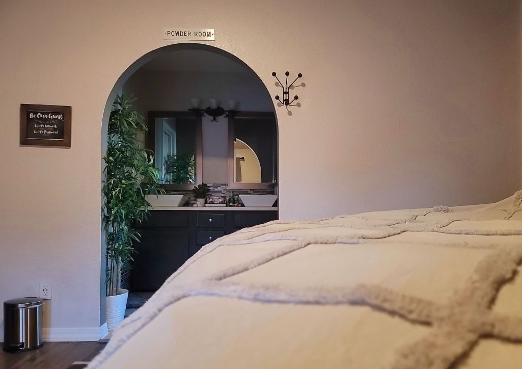 A bedroom with a large bed, a powder room sign, a mirror, and a potted plant.
