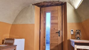 A room with a wooden door, a small table, a chair, and a white refrigerator.