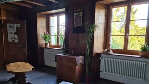 A cozy cabin room with a wooden bench, a dresser, and a bed. There are windows with views of trees and a radiator.
