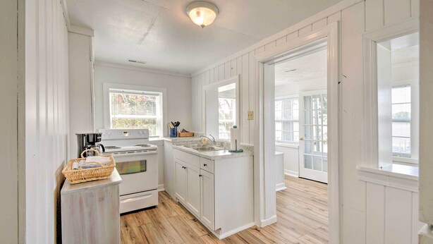 A kitchen with white cabinetry, a wooden floor, and a window with blinds.