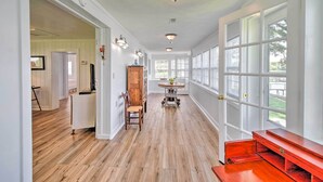 A spacious hallway with wooden flooring, a dining area with a table and chairs, and large windows providing natural light.
