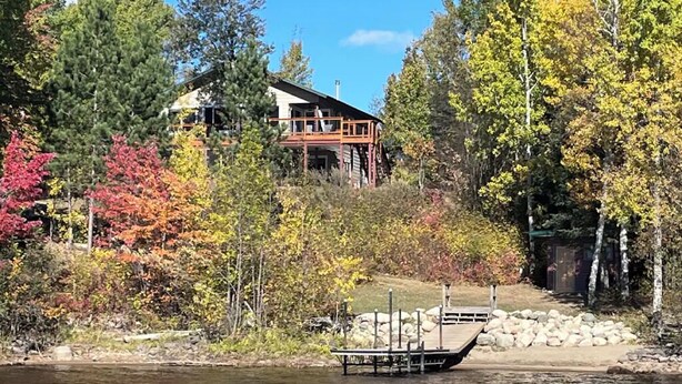 A lakeside cabin with a deck, surrounded by autumn foliage and a dock extending into the water.