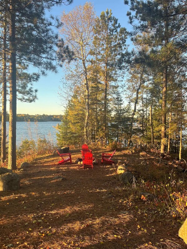 Un terrain de camping avec des chaises Adirondack rouges et une vue dégagée sur un lac.