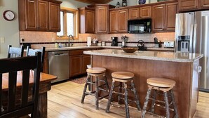 A kitchen with wooden cabinets, a central island with stools, stainless steel appliances, and a wooden ceiling.