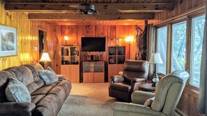 Ein gemütliches Blockhaus-Interieur mit Holzwänden, einem Kamin, einem Fernseher und einer bequemen Sitzecke.