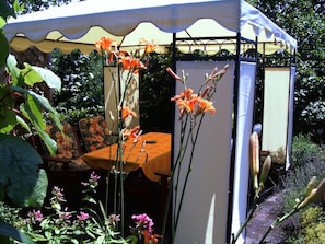 Ein Garten mit einem Pavillon, einem Tisch mit orangefarbener Tischdecke und verschiedenen Blumen.