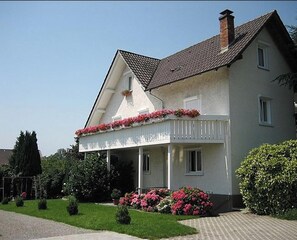 Ein zweistöckiges Haus mit Balkon, Schornstein und einem Blumengarten.