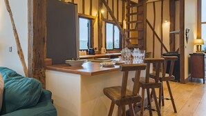 Una cocina rústica con vigas de madera a la vista, una barra de madera y una escalera que sube a un nivel superior.