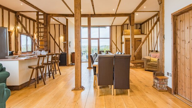 Una habitación amplia con suelo de madera, un comedor con una mesa larga y sillas, y una cocina con mostrador y taburetes.