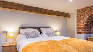 A bedroom with a large bed, two bedside tables, a wooden ceiling beam, and a brick wall. - Customs House by Bloom Stays,  Large house for family groups of up to 20 (Faversham)