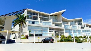 A modern multi-story building with large windows and balconies, surrounded by palm trees and a clear blue sky. - ☺ PUNTAGAVIOTA ☺ HUATULCO ☺ ARROCITO BEACH ☺ (Santa Cruz Huatulco)