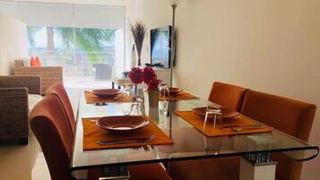 Un comedor moderno con una mesa de vidrio, sillas color naranja y vistas al exterior.