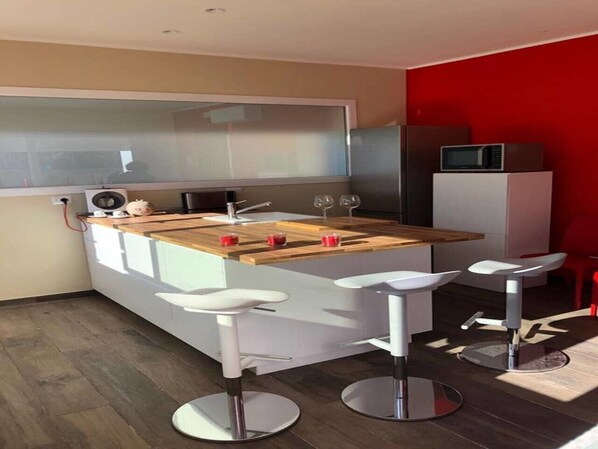A modern kitchen with a wooden countertop, white bar stools, and a microwave on a cabinet.
