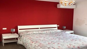 A bedroom with a red wall, a white bed frame, and a patterned bedspread. There are two bedside tables with lamps. - Villa by the sea - in full relaxation - Air conditioned - Wi-fi (Fontane Bianche)
