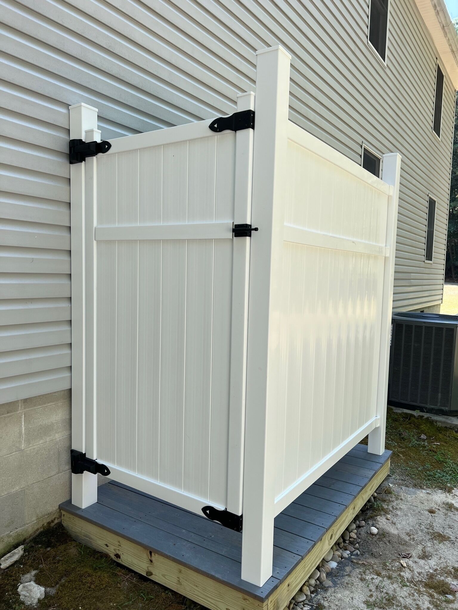 Een witte metalen hek met zwarte scharnieren en een houten terras.