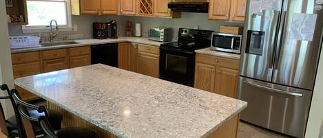 A kitchen with wooden cabinets, granite countertops, stainless steel appliances, and a central island with bar stools.
