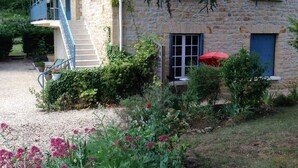 Un edificio in pietra con una scala, un ombrello rosso e un giardino con fiori rosa.