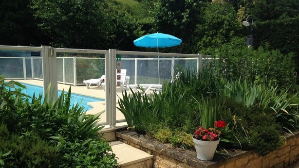 Area piscina con struttura in vetro, ombrellone blu e sedie a sdraio.