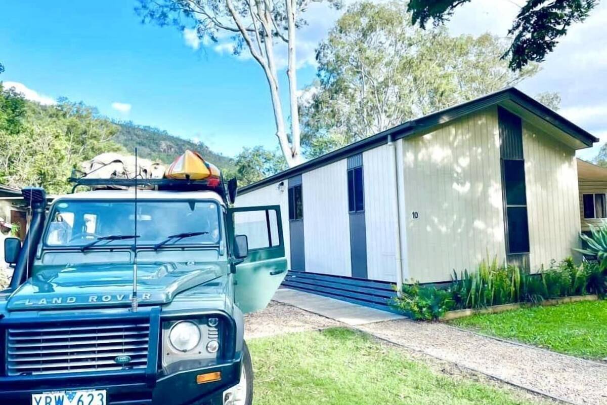 Un Land Rover con un portaequipajes estacionado frente a un pequeño edificio de un piso con el número '10' en la fachada.
