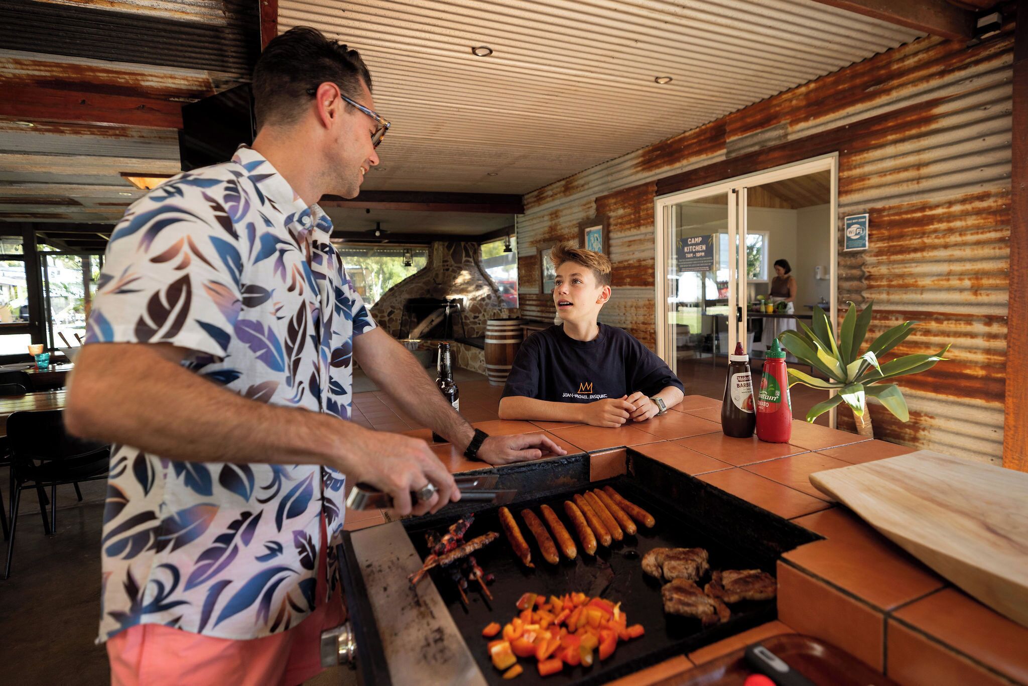 A man grilling sausages and vegetables on an outdoor grill.