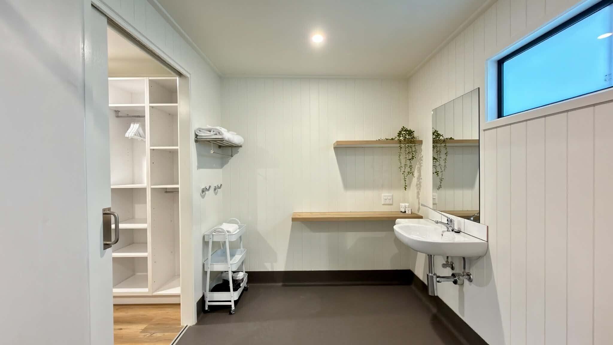 A modern bathroom with a white vanity, a large mirror, and a shower area with a white towel rack.