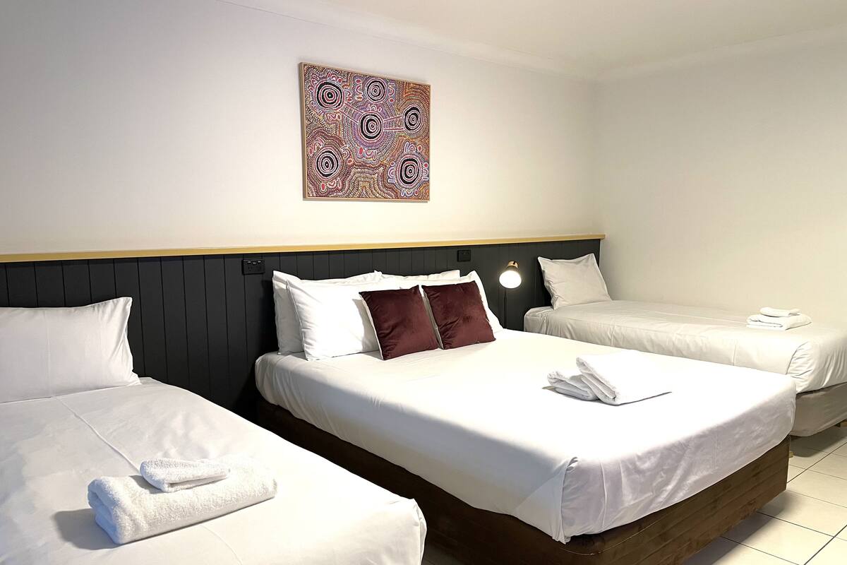 Habitación de hotel con dos camas, cabecera oscura, ropa de cama blanca y una obra de arte colgada en la pared.