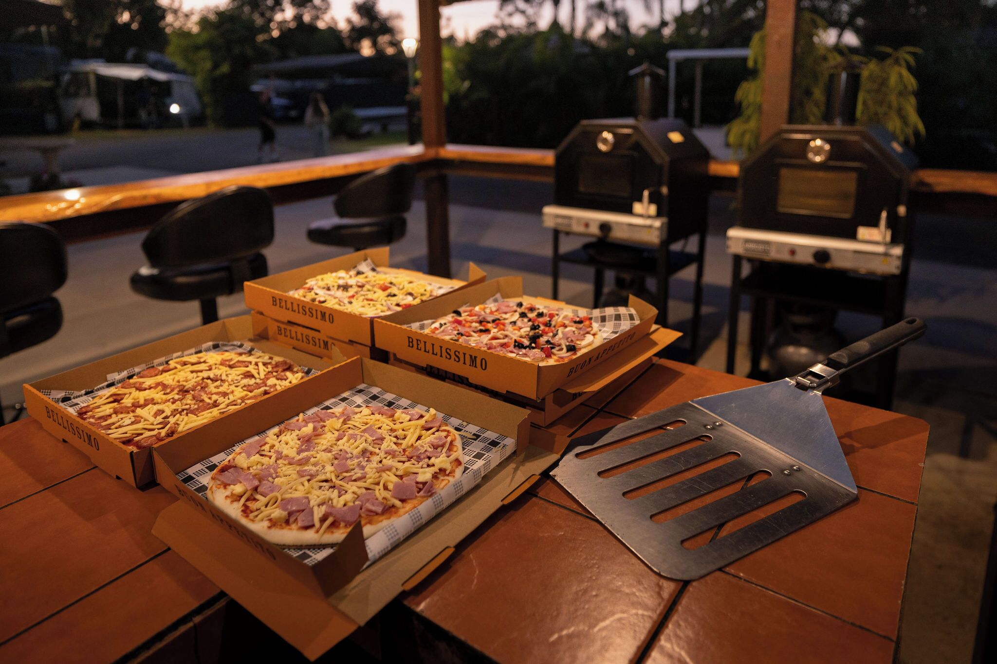 Trois boîtes à pizza sont posées sur une table, avec un coupe-pizza à côté.