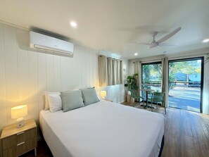 Habitación de hotel con una cama grande, ventilador de techo, equipo de aire acondicionado, ventana con cortinas y vistas al exterior.