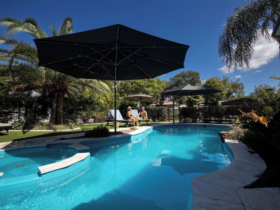 Piscina con sillones de descanso y sombrillas, rodeada de palmeras y follaje.