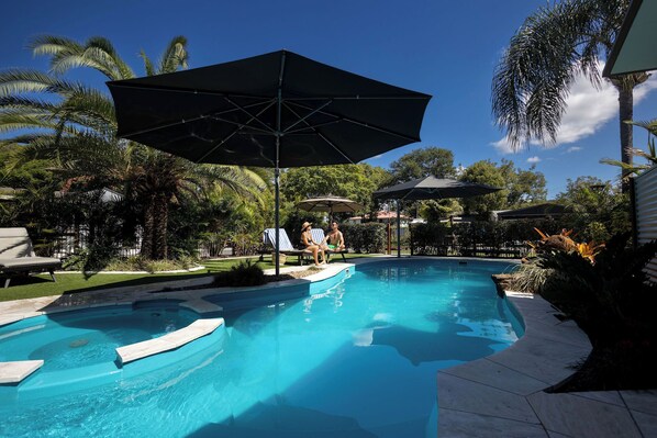 A swimming pool with lounge chairs and umbrellas, surrounded by palm trees and greenery.