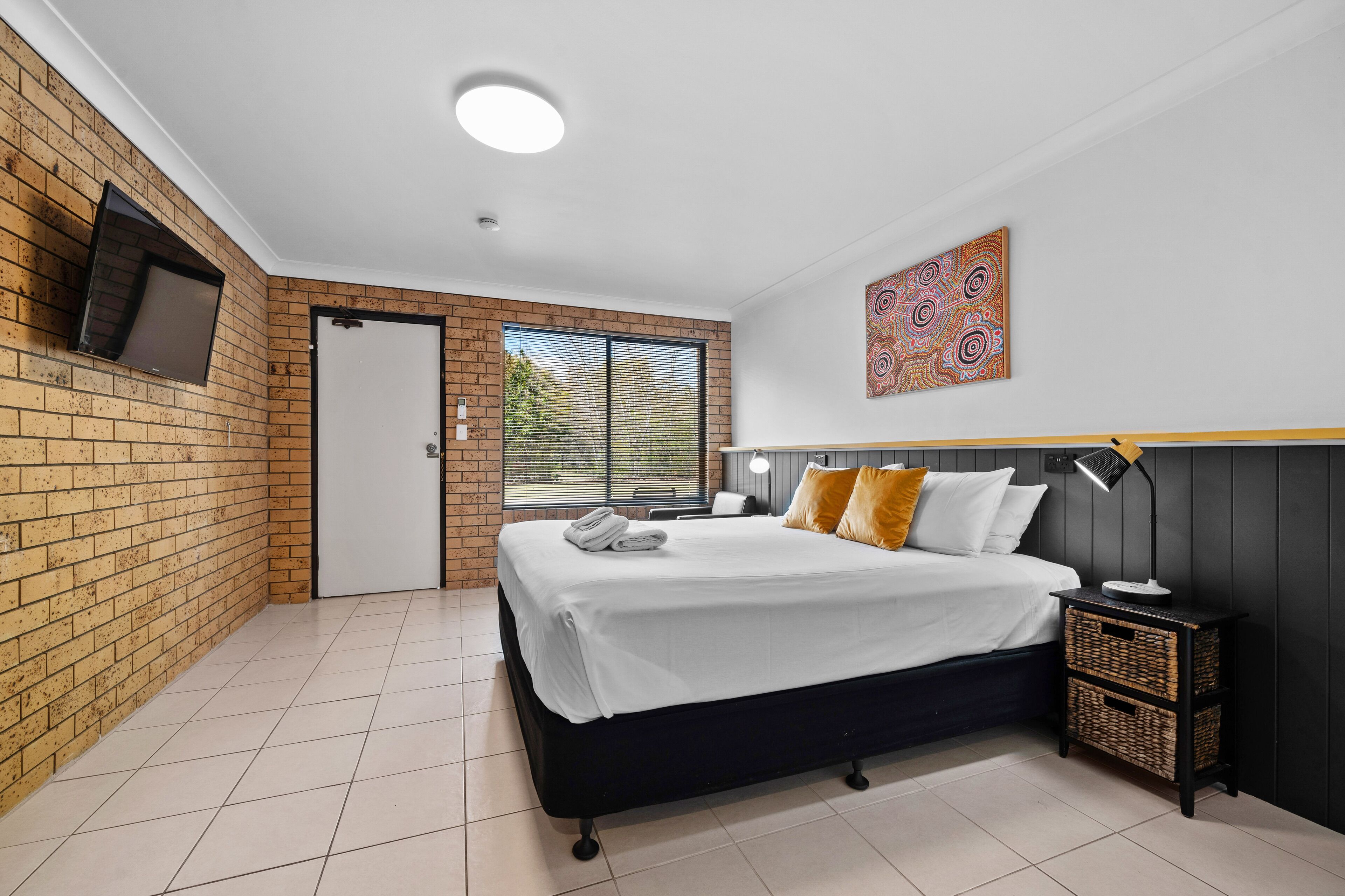 Un dormitorio con cama, televisor montado en la pared, puerta y ventana.