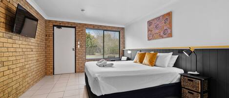 A bedroom with a bed, a TV mounted on the wall, a door, and a window.