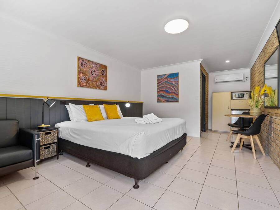 A modern hotel room with a bed, a sofa, a desk, and a kitchenette.