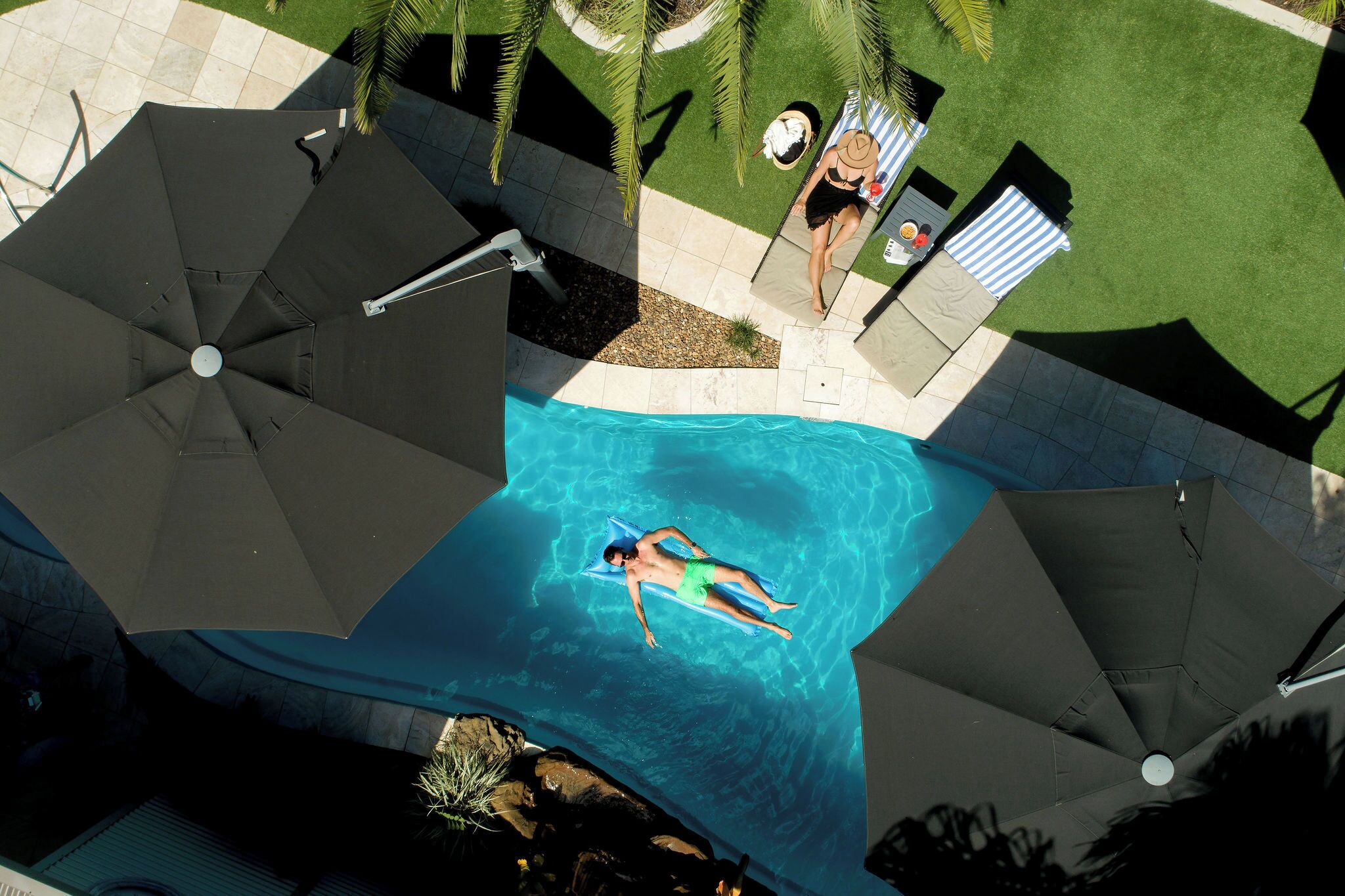 Una piscina con una persona flotando, rodeada de sombrillas y césped.
