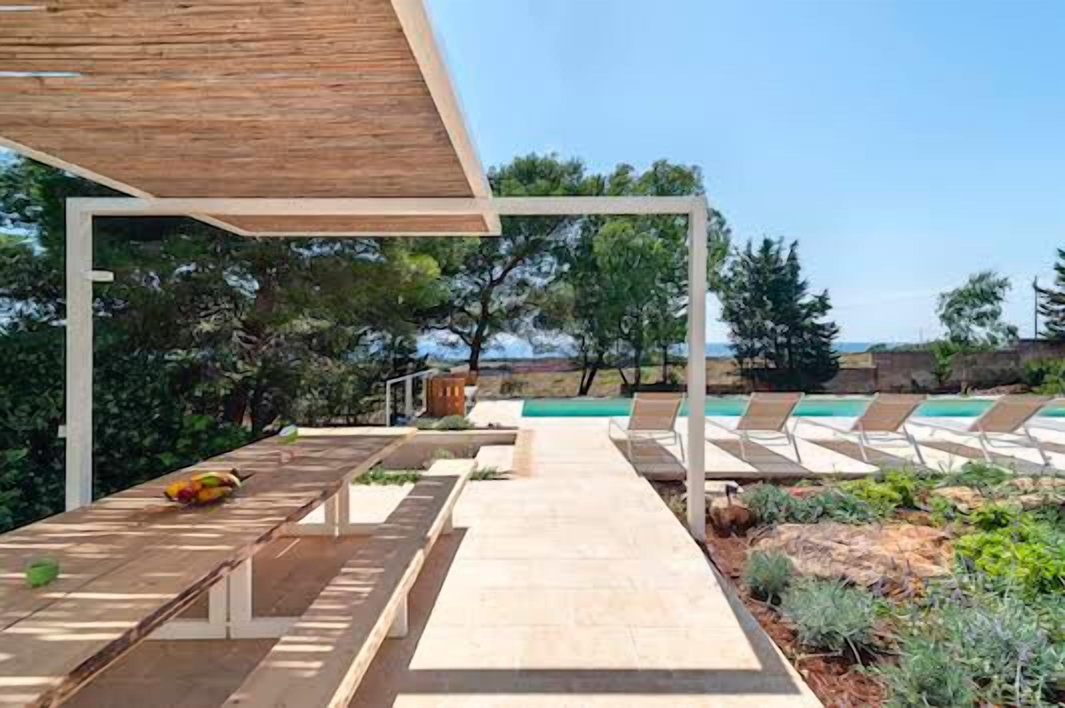 A poolside area with lounge chairs, a wooden pergola, and a pathway leading to a pool.