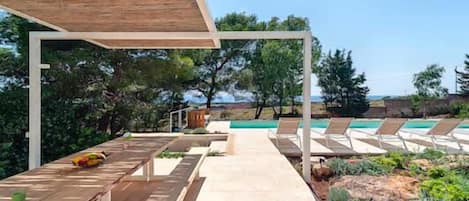 A poolside area with lounge chairs, a wooden pergola, and a pathway leading to a pool.