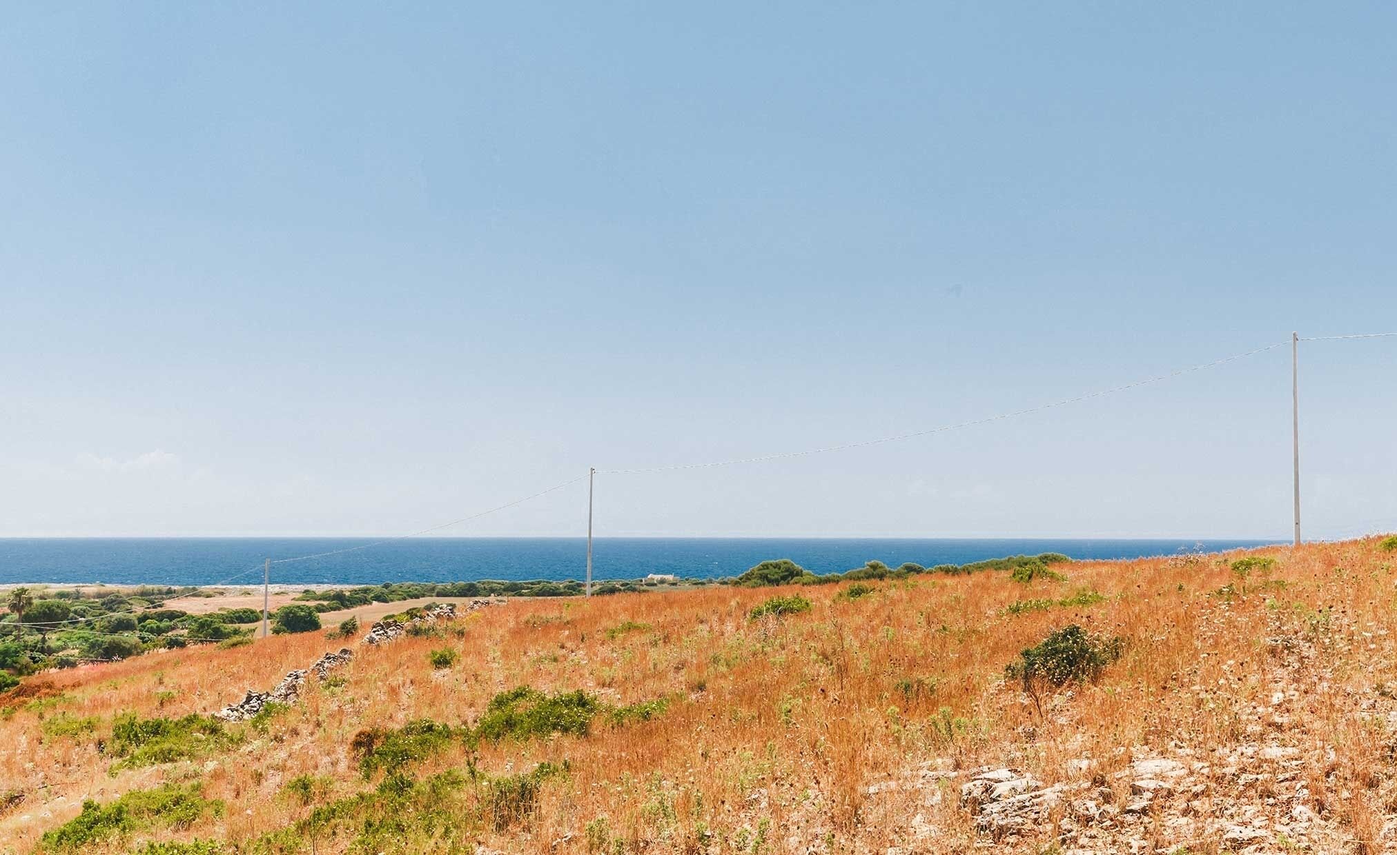 A coastal landscape with a clear sky, a grassy hill, and a distant view of the sea.