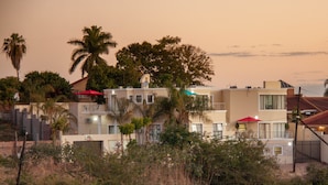 Un immeuble d’habitation doté de nombreux balcons, entouré de végétation et de palmiers.