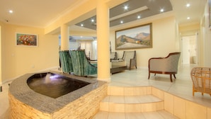 Un vaste espace de vie comprenant un bain à remous en pierre, un tableau représentant un paysage et un coin salon confortable.