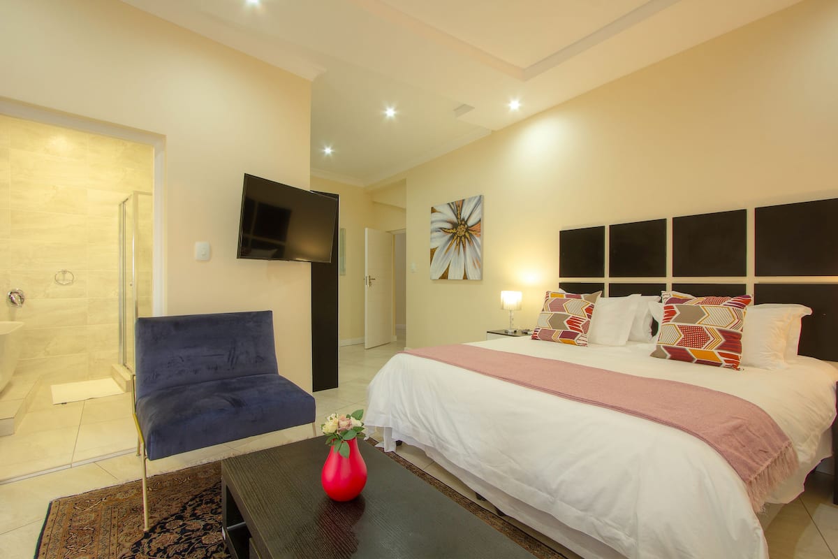A hotel room with a bed, a TV, a shower, and a chair.