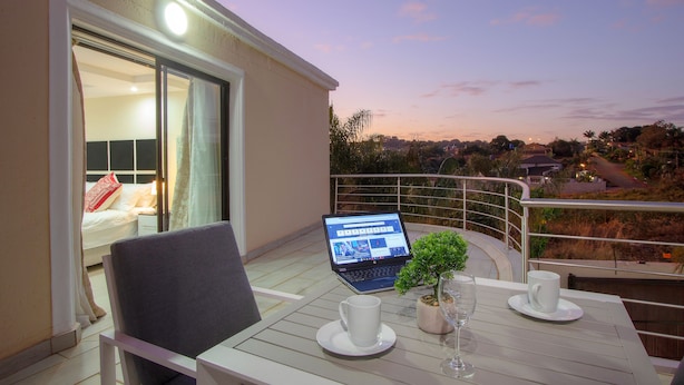 Un balcon avec un ordinateur portable, une petite plante en pot et deux tasses blanches posées sur une table.