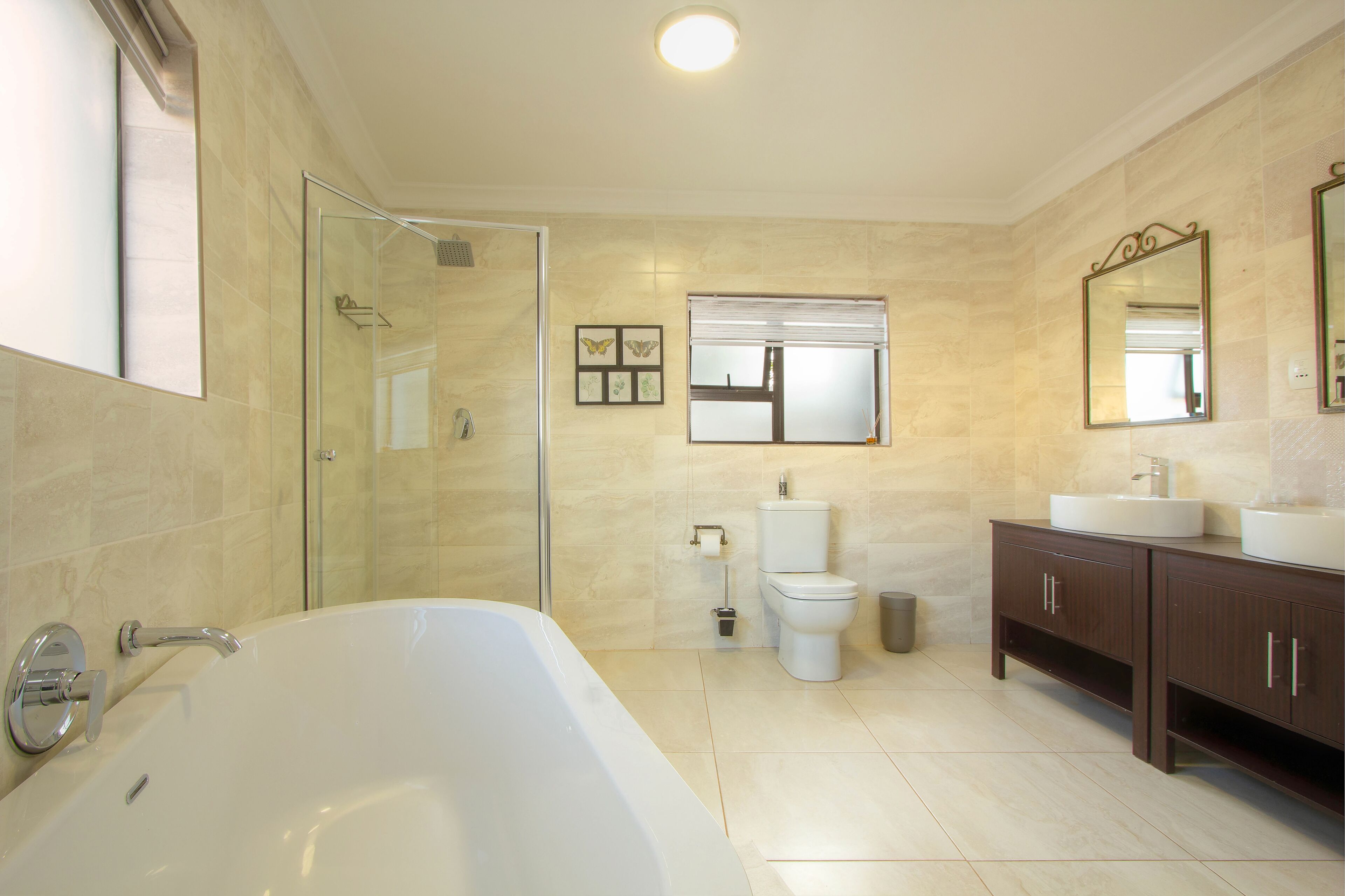 A modern bathroom with a glass-enclosed shower, a large bathtub, a toilet, and a vanity with two sinks.