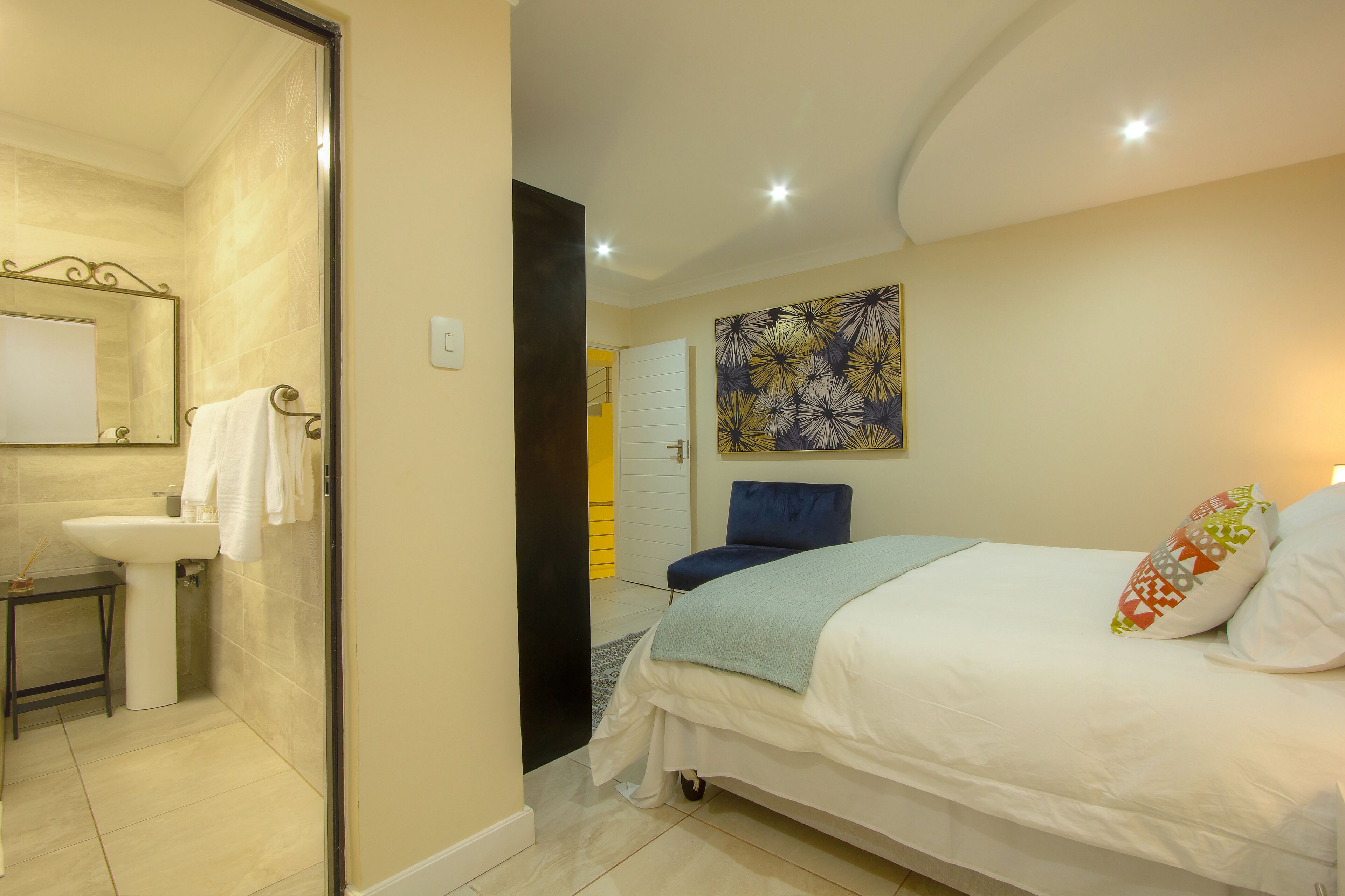 Een slaapkamer met een bed, nachtkastje, raam en een deur die leidt naar een badkamer.