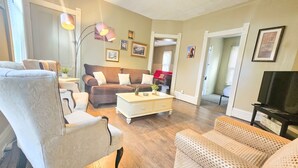 Un salon avec un canapé marron, des fauteuils blancs, une table basse et un meuble pour la télévision.