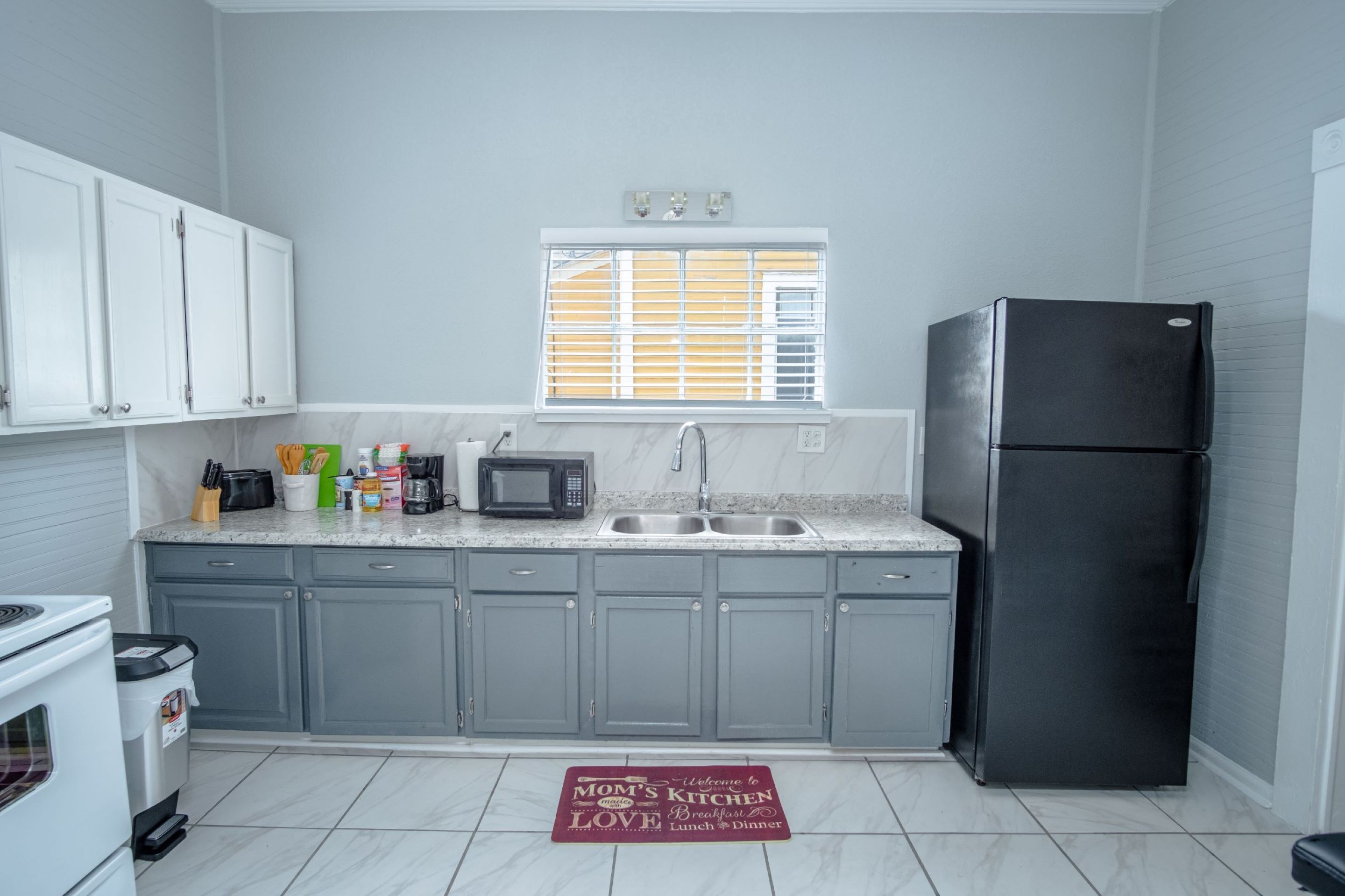 A kitchen with grey cabinets, a black refrigerator, a microwave, and a sink.