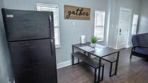 A modern kitchen with a black refrigerator, a wooden sign saying "gather with grateful hearts," a small table with a bench, and a potted plant. - Classic 1br/1ba Charming Apt w/ Modern Upgrades (San Antonio)