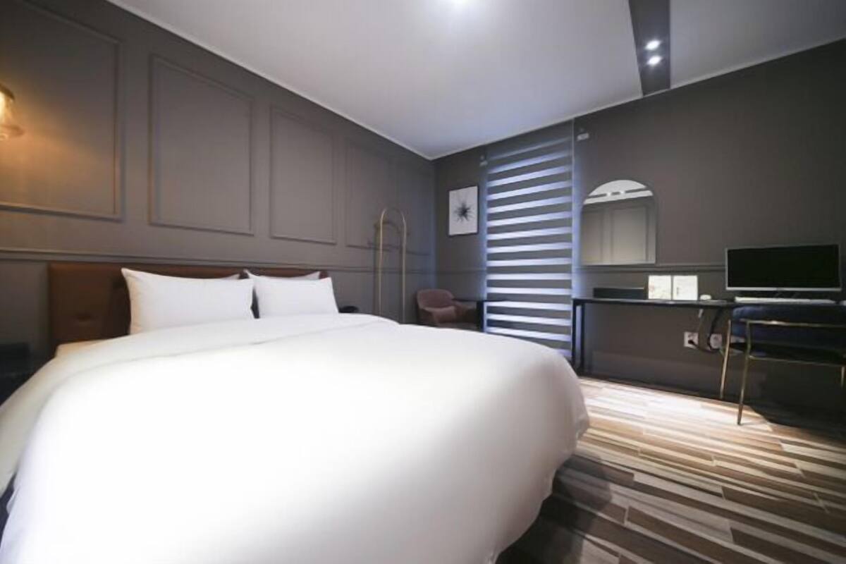 Ett modernt hotellrum med en stor säng, ett skrivbord med en dator, en stol och en TV.