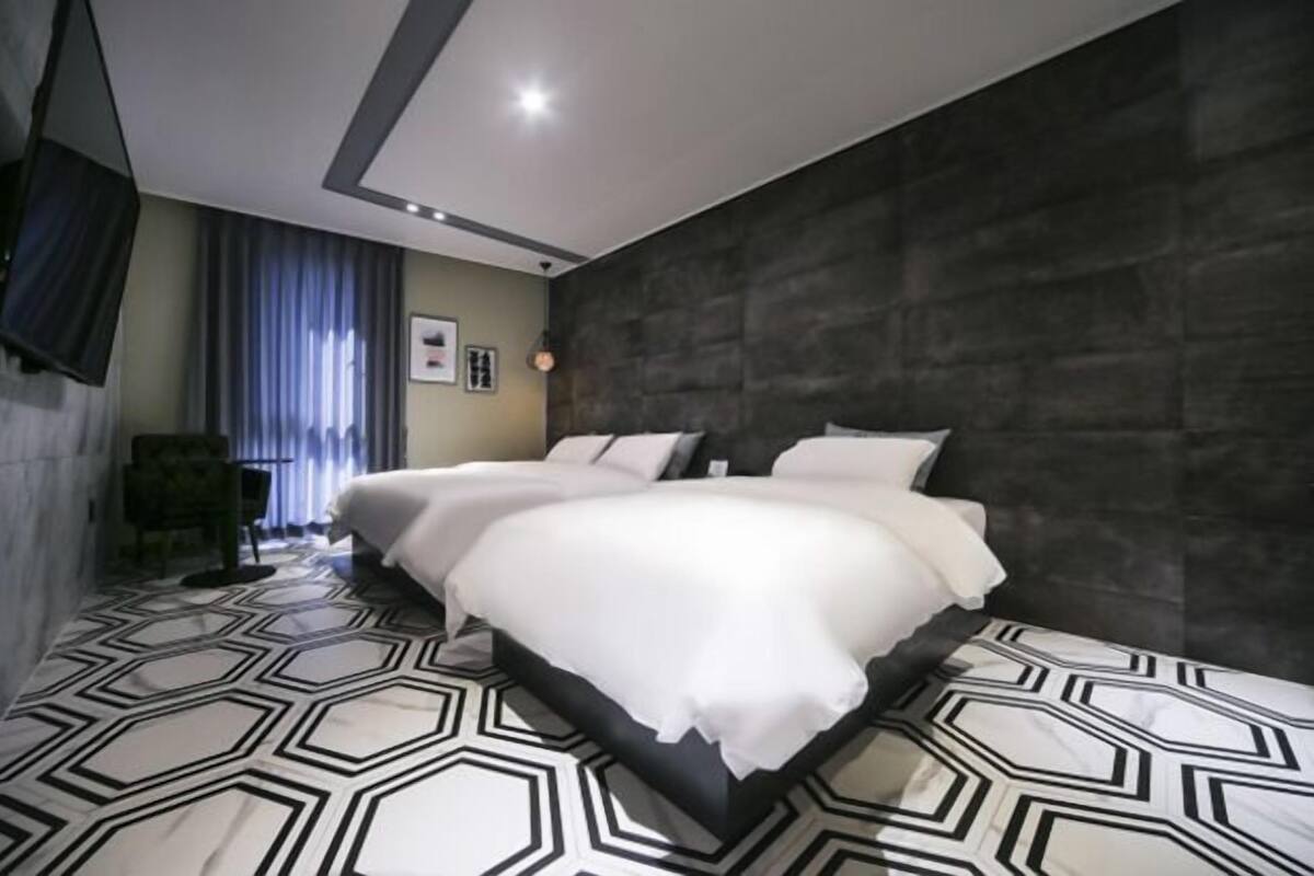 Ett modernt hotellrum med en stor säng, en mörk vägg med tydlig struktur och ett golv med geometriskt mönster.