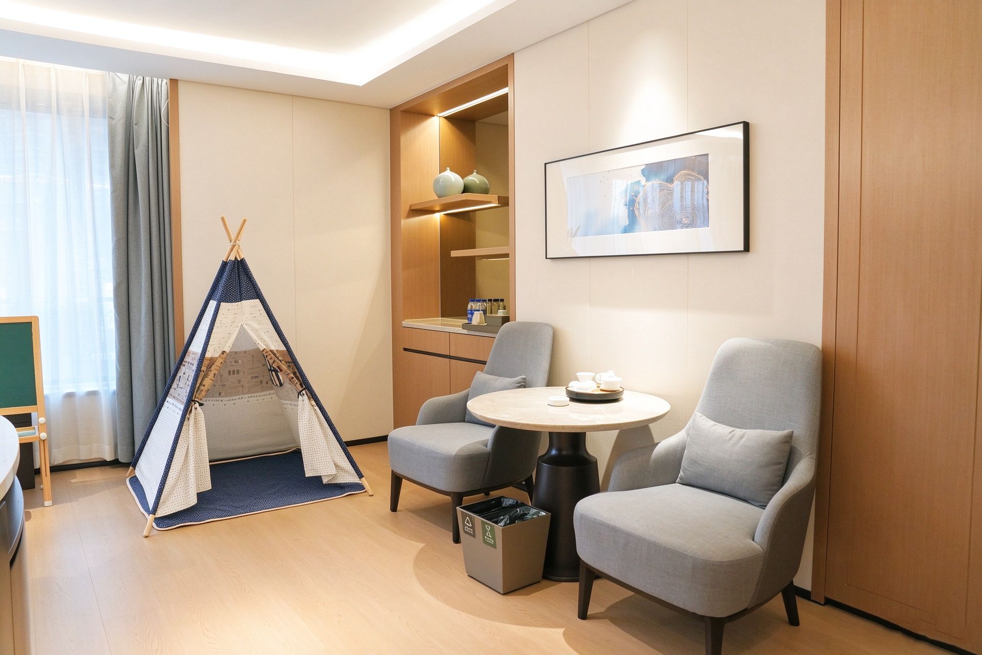 A modern hotel room with a seating area, a small table, a teepee, and a framed picture on the wall.