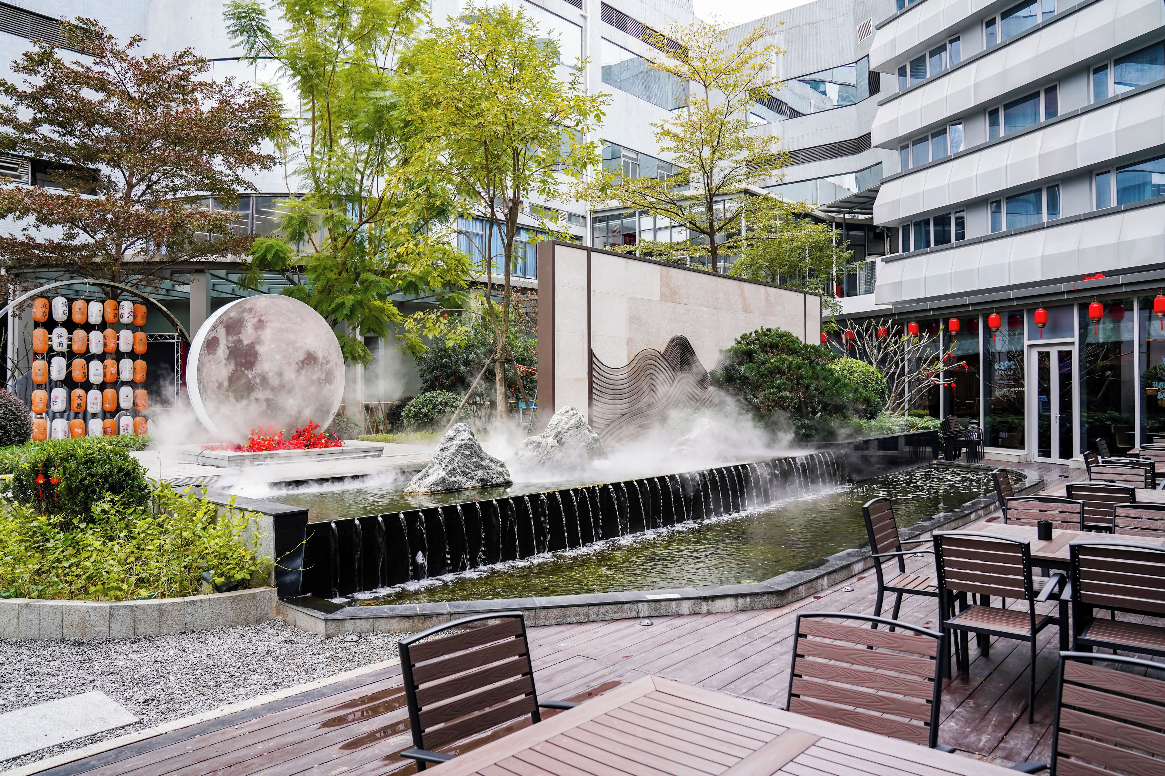 A modern outdoor area with a water feature, seating, and a large moon sculpture.